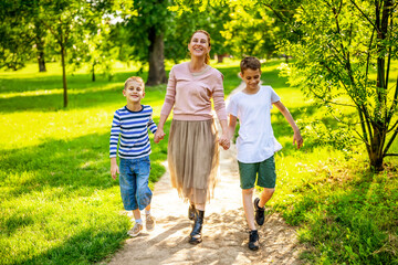 Fototapeta premium Happy mother is walking with her sons in park. They are holding hands and enjoying summer day.