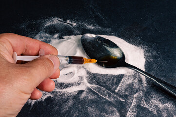 Drug addiction concept. The syringe is filled with heroin prepared in a spoon. Dark background