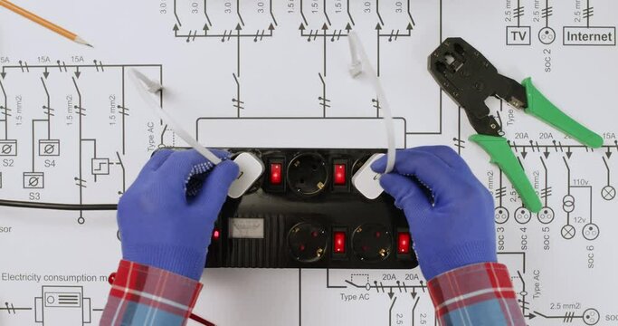 Electrician with assistant plug power banks to socket extension on electrical schematic diagram view from above. Charging devices on network plan