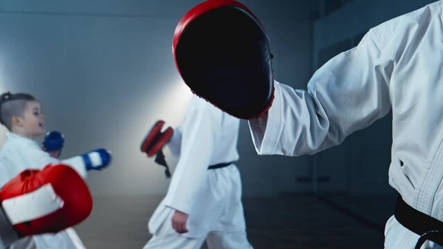 Group of children practicing karate skills in smoky room, performing leg kicks, punches. Focus mitts. Children follows instructions of their instructor, showcasing discipline and control