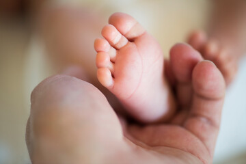 Parent holding small feet of little baby lying on bed.