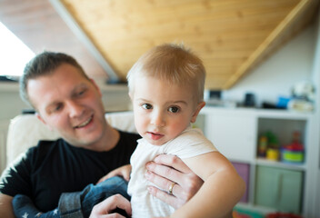 Father holding his son in arms, spending time with toddler in his room. Unconditional paternal love, Father's Day concept.