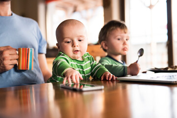 Father sitting at table with two sons, small baby and older brother eating porridge. Unconditional parental love, family moment.