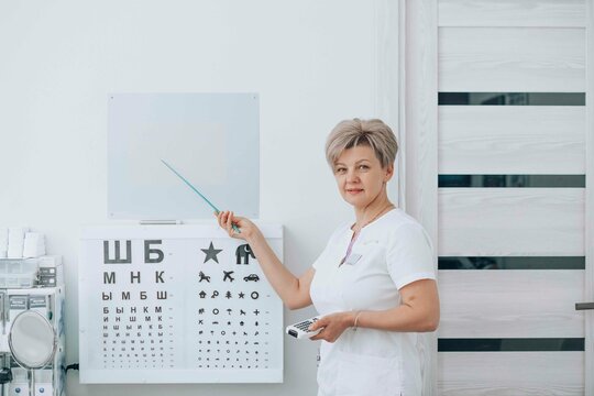 Smiling ophthalmologist holding remote control and pointing with stick on eye chart