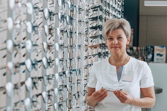 Smiling ophthalmologist standing near eyeglasses rack at store