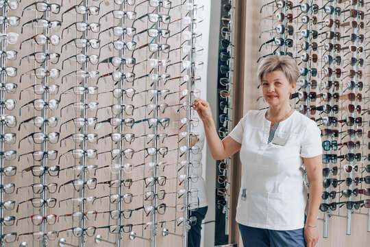 Smiling ophthalmologist standing near eyeglasses rack at retail showroom