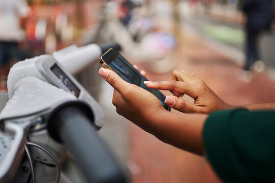Hands of businesswoman unlocking bicycle through mobile phone scanning at parking station