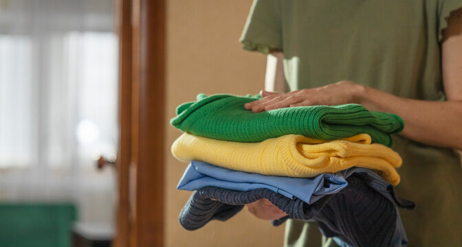 Woman holding stack of folded clothes at home