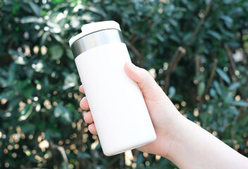 Young woman holding thermos mug against green plants background.