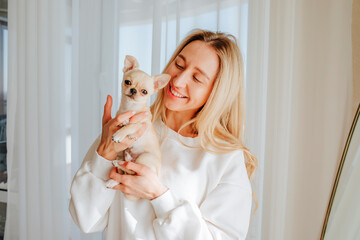Smiling young woman holding chihuahua dog at home