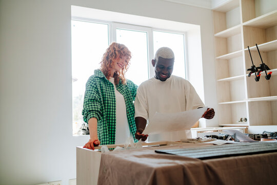 Happy young man and woman reading instruction manual at table in new home