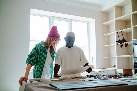 Happy man and woman reading instruction manual at table in new home