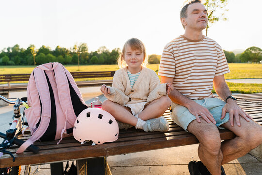 Father and daughter doing meditation on bench in park - Powered by Adobe