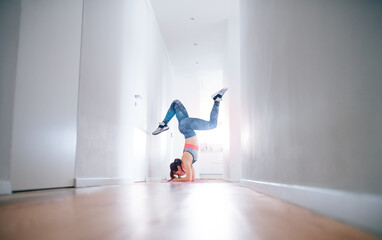 Beautiful redhead woman doing headstand during home fitness routine. Home workout on gym mt in living room, sporty woman wearing sportswear.