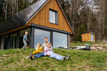 Happy family on grass in front of modern house spending leisure time together