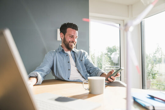 Smiling businessman using smart phone at desk in home office