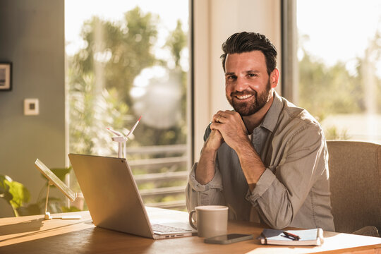 Happy businessman sitting with laptop at desk in home office
