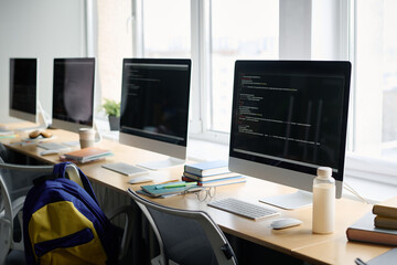 No people shot of computers with codes on screen on desks in modern classroom, copy space