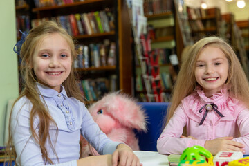 Two funny girls are reading books in the library. Wooden alphabet blocks