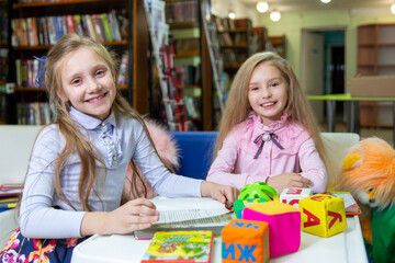 Two funny girls are reading books in the library. Wooden alphabet blocks