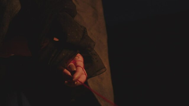 A woman in vintage clothing in the dark with her hands tied with black cloth holds a red thread of hope. Soft light on hands. Psychological problem