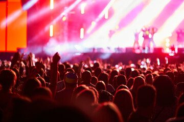 Concertgoers enjoy live music at outdoor fest, vibrant stage lights illuminate performers. Fans...