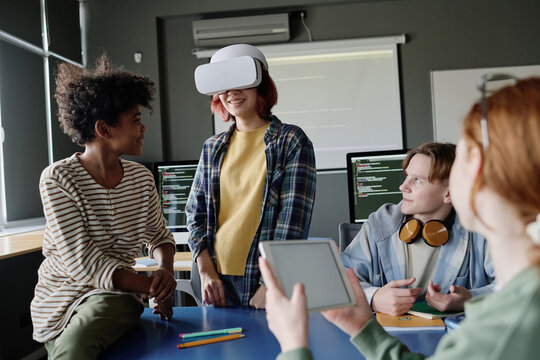 Group of ethnically diverse teen students working together on software for VR headset with use of digital tablet
