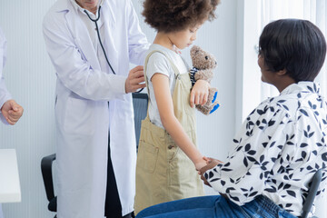 Obraz premium Professional team pediatrician examining young patient girl in hospital. Child standing, being comforted by guardian holding mother's hand. Doctor preparing medical instrument, child's health care
