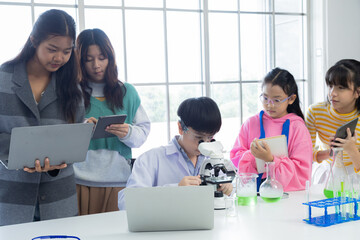 Group of students in science class using laptops and microscopes, conducting experiments. Young diverse pupils focused on research and senior teacher supervision. educations and back to school concept