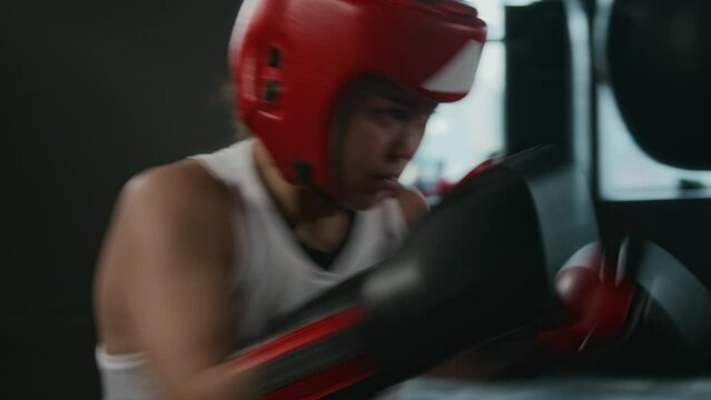 Medium handheld shot of two young female boxers in blue and red padded safety gear having vigorous sparring at gym, delivering strong jabs at opponent and guarding from blows