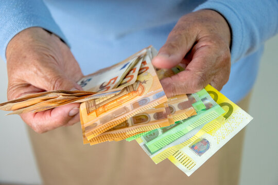 A person is holding a stack of euro banknotes in their hand. The bills are folded and fanned out, with the 50 euro note visible on top