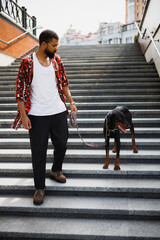 Stylish african american man walking with doberman dog on stairs in city