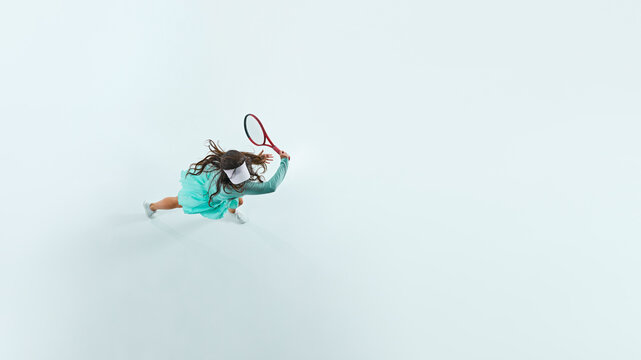 Aerial view of young, athletic woman with tennis racket training her skills in motion on white studio background. Concept of professional sport, championship, active lifestyle, tournament. Ad - Powered by Adobe