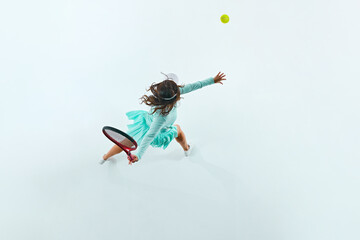 Aerial perspective. Female tennis player in turquoise sportswear serves ball against white studio...