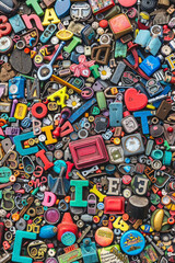 Fototapeta premium A crowded assortment of fridge magnets in various shapes, sizes, and colors, filling the entire frame. The magnets include letters, numbers, and novelty designs.