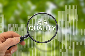 Air Quality concept with hand holding a magnifying glass with written text against a cityscape
