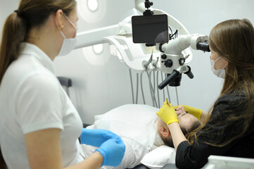 dentist working with dental microscope in modern stomatology clinic. Doctor using microscope for root canal treatment. Stomatologist performs a surgical operation. Cosmetic dentistry and surgery.