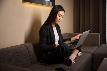 Satisfied female looking at laptop and holding ticket and phone in hands