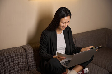 Beautiful smiling woman working with laptop on sofa in hotel room