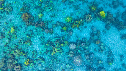 Top view. Summer sea water, blue surface. The water is clear with ripples and sparkles in the sunlight and you can see coral under the sea	
