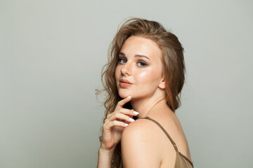 Fototapeta premium Nice female model with make-up, clear skin and long wavy hairstyle posing on white background. Fashion beauty studio portrait of young woman