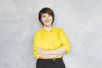 Smiling businesswoman in yellow shirt looking at camera standing on grey background