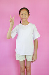 Portrait of Asian girl child showing victory sign fingers isolated on pink studio background.