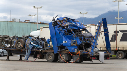 Dented blue truck cab and a semi-trailer on a tow platform in the parking lot after a serious...