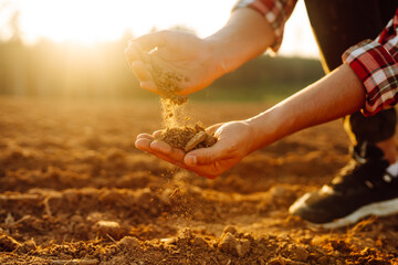 Close up of the farmer hands touching dry ground in an agricultural field while analyzing soil during the summer day. Organic gardening, agriculture.