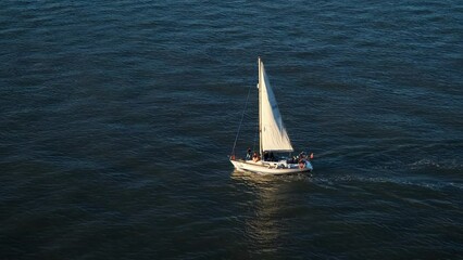 Wind sailing boat sailing in the sea, river, lake water in golden hour sunny day. Top aerial view on a small fishing ship. Ocean vacation, relaxing, chill time on a yacht. Summer holidays in Portugal
