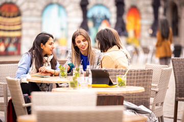 Three women friends chatting and laughing at an outdoor cafe on a beautiful day, enjoying each others company