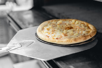 Pizzamaker worker puts pizza into an electric oven, business pizzeria concept