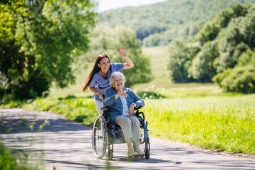 Female caregiver pushing senior woman in wheelchair. Nurse and elderly woman enjoying a warm day in...