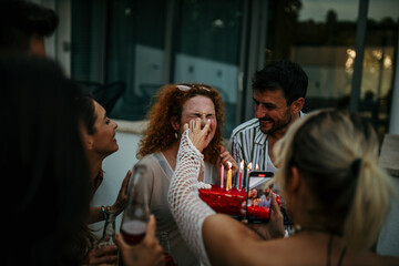Cute diverse friends making surprise for excited birthday lady, holding birthday cake and smiling